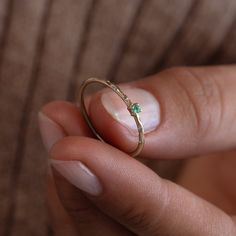 a woman's hand holding a gold ring with a green diamond on it,