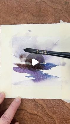 a person is holding a pen and drawing on paper with watercolors in front of them