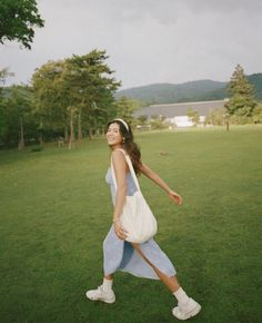 a woman walking across a lush green field with trees in the backgroung