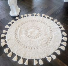 a white round rug with tassels on the floor next to a vase and lamp