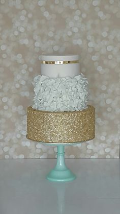 a three tiered cake with white and gold frosting on a blue pedestal in front of a polka dot wall