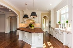 a large kitchen with wooden floors and white cabinets on the walls, along with two pendant lights hanging from the ceiling