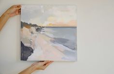 two hands are holding up a painting on the wall with white and gray colors,