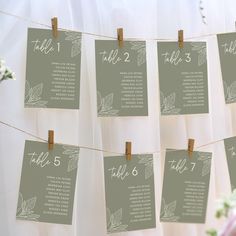 wedding seating chart hanging on clothes line with flowers in vases behind it and table number cards attached to the strings