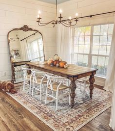 a dining room table with white chairs and a dog laying on the floor in front of it