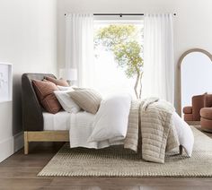 a bed with white sheets and pillows in a bedroom next to a large round mirror