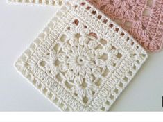 two crocheted squares are sitting on a table top, one is pink and the other is white