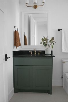 a white toilet sitting next to a green cabinet in a bathroom under a large mirror