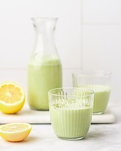 three glasses filled with green smoothie next to lemons and a pitcher on a counter