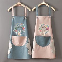 two aprons are hanging on the wall, one has an embroidered name and the other has flowers