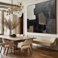 a dining room table with white chairs and a large painting on the wall above it