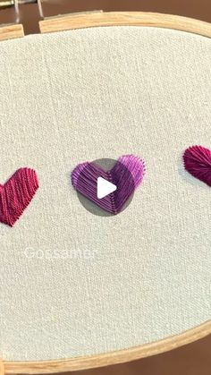 three hearts are stitched together on a white piece of fabric with pink and purple yarn