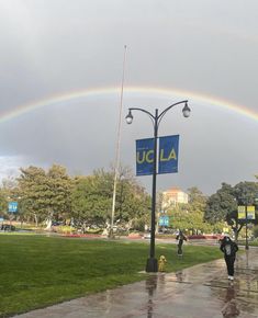 a rainbow in the sky over a park with people walking on it and a sign that says ucla