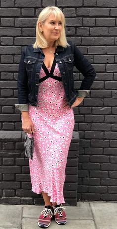 a woman standing in front of a brick wall wearing a pink dress and jean jacket