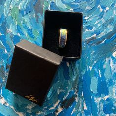 an open ring box sitting on top of a blue and white painting covered tablecloth