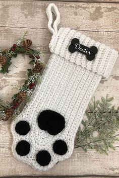 a crocheted stocking with black and white paw prints on it, next to a wreath