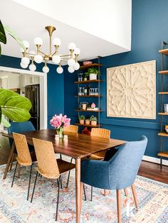 a dining room with blue walls and wooden table surrounded by chairs, potted plants and bookshelves