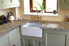 a kitchen with marble counter tops and white cupboards next to a window that has a potted plant in it