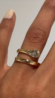 a woman's hand with two gold rings on top of her finger and an oval shaped diamond in the middle