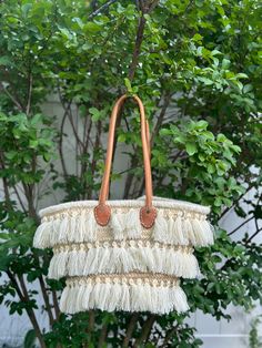 Discover the perfect blend of traditional craftsmanship and contemporary style with this stunning handmade Moroccan raffia bag. This beautiful piece features intricate woven patterns and eye-catching fringe detailing, showcasing the exceptional skill of Moroccan artisans. The bag is adorned with three tiers of elegant fringe, adding a playful yet sophisticated touch. Sturdy leather handles provide a comfortable carry, making it ideal for everyday use or special outings. Each bag is a unique creation, ensuring you have a one-of-a-kind accessory to complement any outfit. Features: *Artisan-crafted in Morocco *High-quality raffia material *Three tiers of fringe detailing *Durable leather handles *Unique, one-of-a-kind design Ideal For: *Beach trips *Shopping *Casual outings *Enhancing bohemia Natural Bucket Bag With Braided Handles For Market, Natural Color Bags With Tassels For Vacation, Natural Color Vacation Bags With Tassels, Natural Shoulder Bag With Braided Handles For Shopping, Handwoven Basket Shoulder Bag For Vacation, Bohemian Beach Bucket Bag In Natural Fiber, Brown Tassel Beach Bag For Vacation, Natural Tassel Beach Bag For Vacation, Natural Beach Bag With Tassels For Vacation