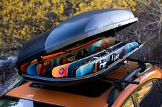 an orange car with surfboards on the roof rack and trees in the back ground