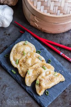 two dumplings on a slate with chopsticks next to it and some garlic