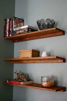 two wooden shelves with books and candles on them in a room that has gray walls