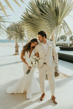 a bride and groom standing next to each other in front of palm trees at the beach