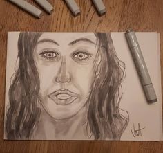 a pencil drawing of a woman's face on paper next to markers and pens