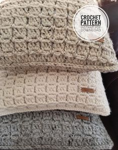 two crochet pillows sitting on top of a couch next to each other, one is white and the other is gray