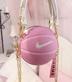 a pink purse with a basketball hanging from it's side on a white bed