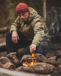 a man is cooking food over an open fire in the woods with rocks and logs