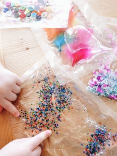 two children are making crafts with plastic bags and sprinkles on the table