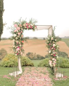 an outdoor wedding ceremony with flowers and greenery on the aisle, in front of a field