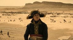 a man wearing a hat standing in front of a large group of people on the desert