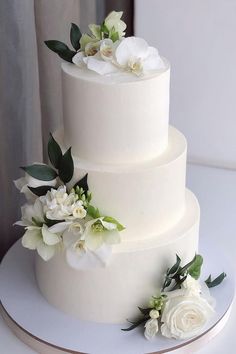 a three tiered cake with white flowers and greenery