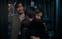 two men hug each other in front of a mirror while another man looks at them