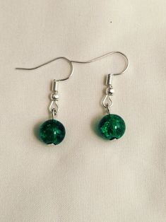 two green glass beads hanging from silver earwires on a white cloth covered surface