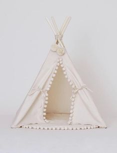 a white teepee with pom poms on the front and bottom, sitting in front of a white background