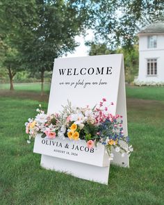 a welcome sign with flowers on it in the grass