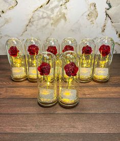 six glass vases with red flowers in them on a wooden table next to a marble wall