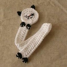 a crocheted white cat laying on top of a bed next to a pillow