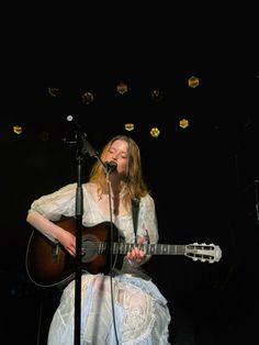 a woman in white dress playing guitar on stage