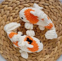 two orange and white knitted koi fish sitting on top of a woven mat