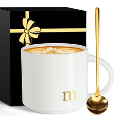 a cup of coffee with a spoon in it next to a black box and gold ribbon