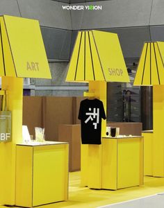 some yellow stands with umbrellas and shirts on them in a store display area at an art fair