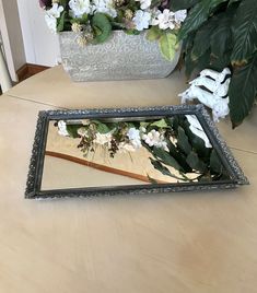 a mirror sitting on top of a wooden table next to a potted plant with white flowers