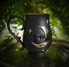 a black coffee mug with a crescent moon and stars on the side sitting on a metal tray