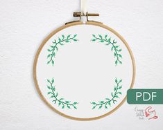 a cross stitch wreath is hanging on the wall next to a small hoop with green leaves