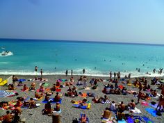 many people are on the beach and in the water, some have sunbathers